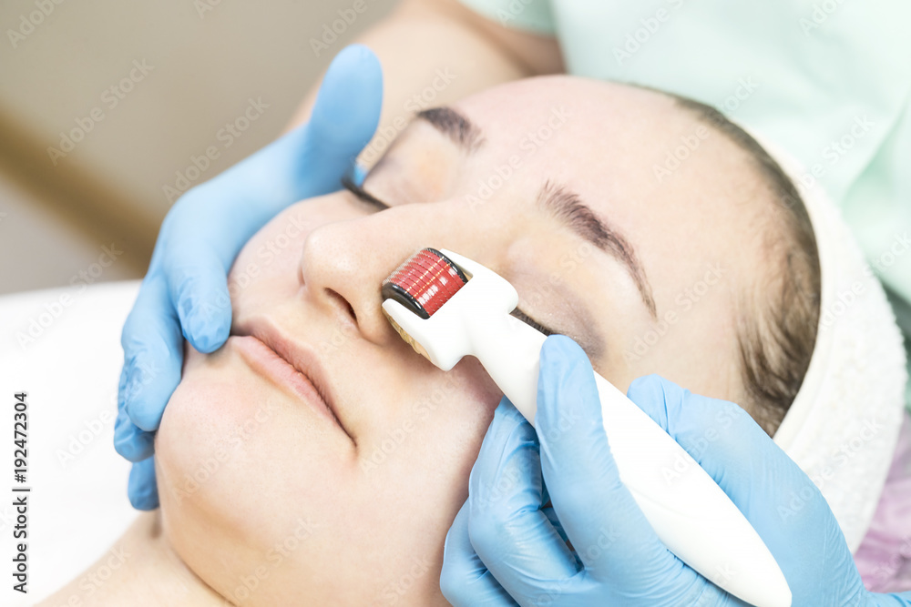 The woman undergoes the procedure of medical micro needle therapy with a modern medical instrument derma roller 