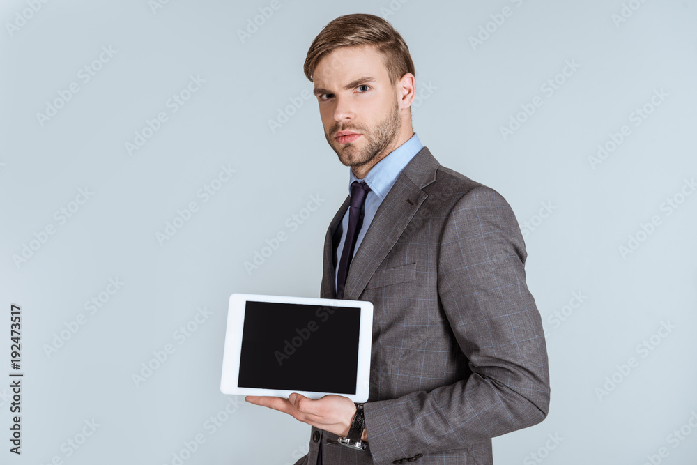 Young thoughtful businessman presenting digital tablet isolated on grey Young thoughtful businessman presenting digital tablet isolated on grey