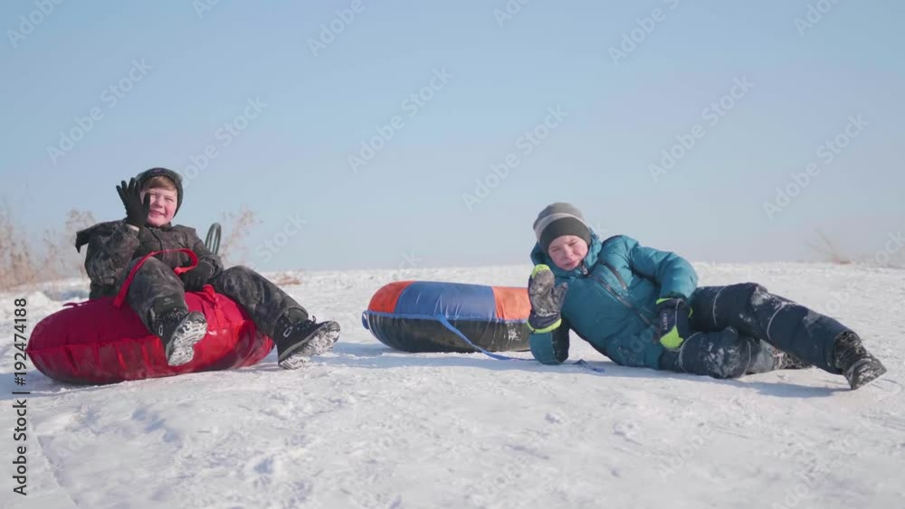 Two children ride on a snowy hill on a sled. Children sit on top of the mountain. Sport and outdoor activities Two children ride on a snowy hill on a sled. Children sit on top of the mountain. Sport and outdoor activities