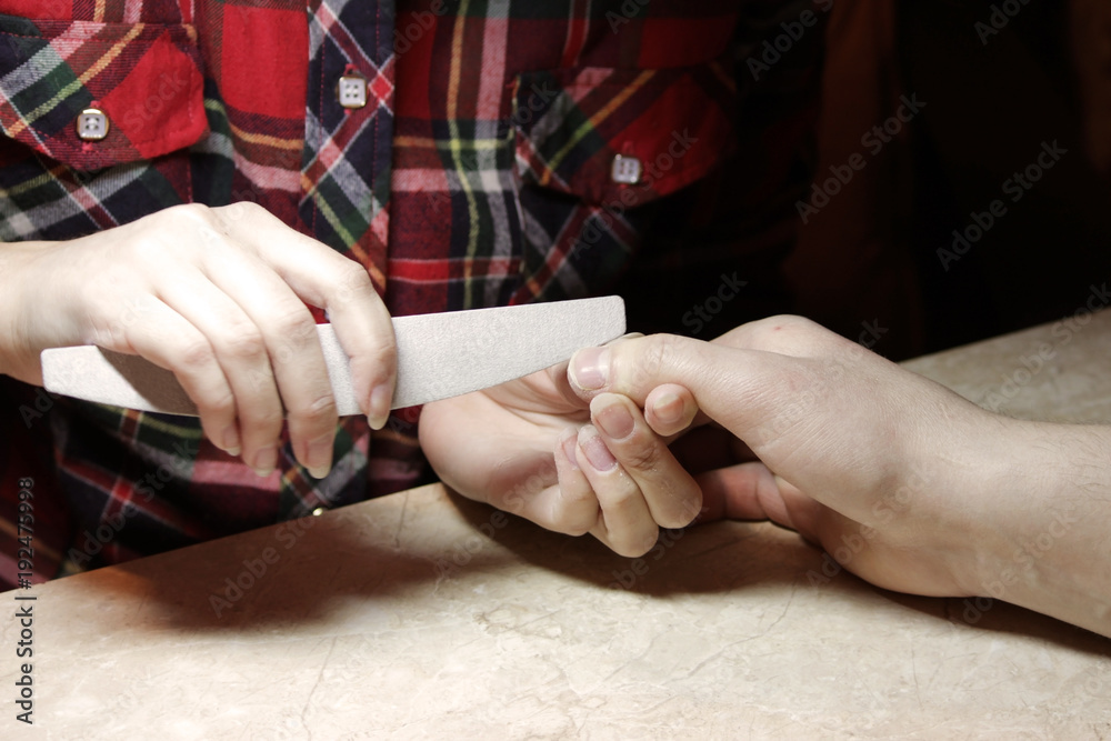 Obraz premium A student at the training courses of a manicure gives shape to nails the hand of a man client with a saw of a buff.