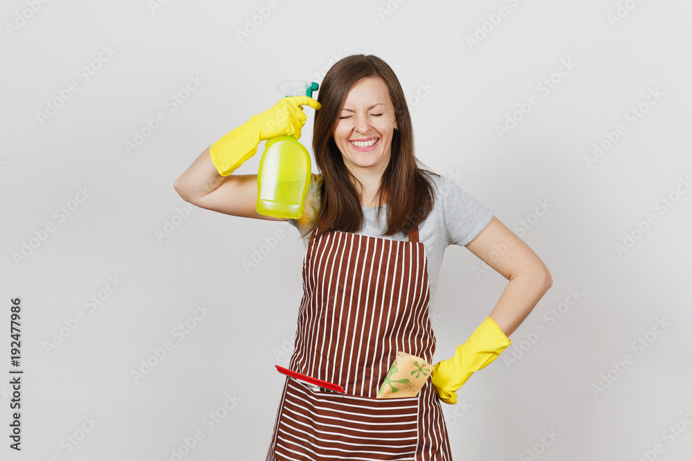 Young fun housewife in yellow gloves, striped apron, cleaning rag, squeegee in pocket isolated on white background. Housekeeper woman shoots from spray bottle with cleaner liquid. Bottle copy space. Young fun housewife in yellow gloves, striped apron, cleaning rag, squeegee in pocket isolated on white background. Housekeeper woman shoots from spray bottle with cleaner liquid. Bottle copy space.
