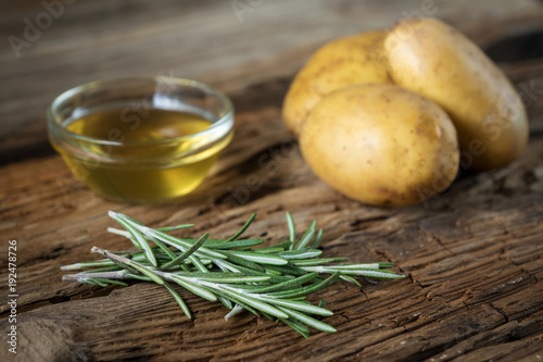 potato tubers, rosemary, olive oil on wooden background