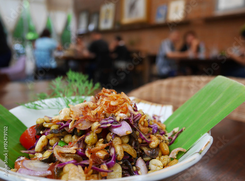 Closeup of Burmese Tea Leaf Salad or Lahpet in a white plate with banana leaf on a dark wooden table with blurry restaurant background