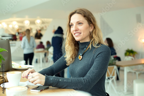 Woman is sitting in a cafe in front of a window.