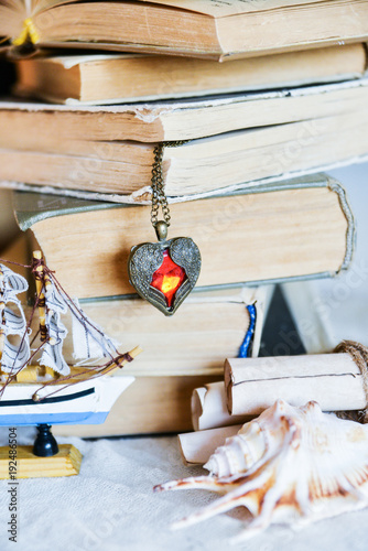 stack of old books, heart-shaped pendant, old scrolls, seashell - the concept of adventurers, travelers, dreamers and treasure hunt