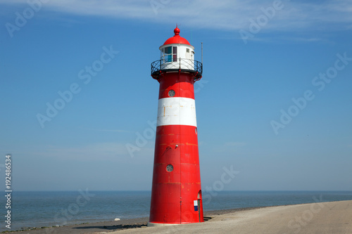 Red lighthouse on a dike seawall by the blue sea