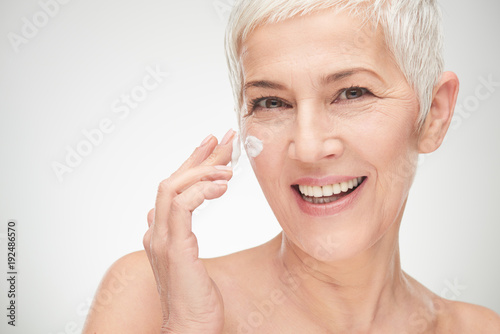 Head shot of beautiful senior woman putting on the creme.