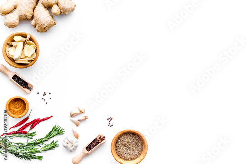 Colorful dry spices in bowls and spoons near ginger, garlic, rosemary on white background top view copy space