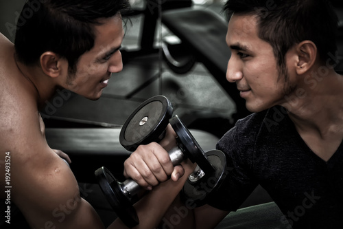 Two Asian men use dumbbell exercise weight-lifting arm-wrestle compete in fitness gym