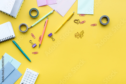 Scattered stationery on student's desk. Yellow background top view copy space