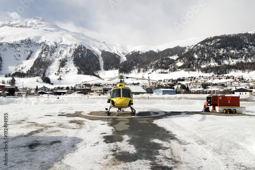 A yellow tour helicopter getting fuel in heliport in the alps switzerland in winter