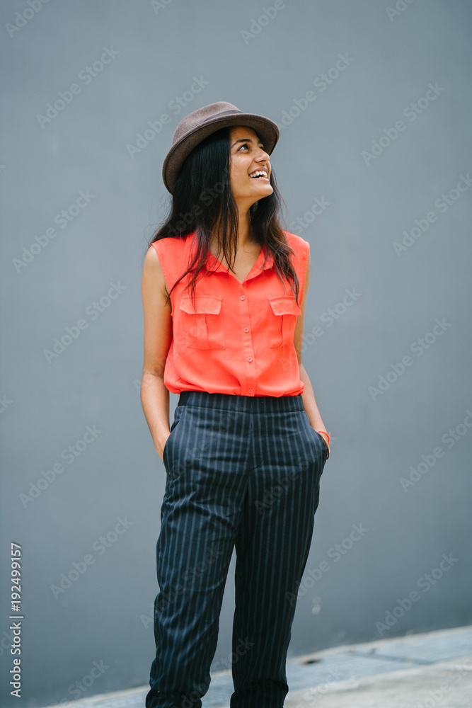 Attractive young professional Indian woman looking up and smiling. She is dressed casually with her hands in her pockets against a grey background. Attractive young professional Indian woman looking up and smiling. She is dressed casually with her hands in her pockets against a grey background.