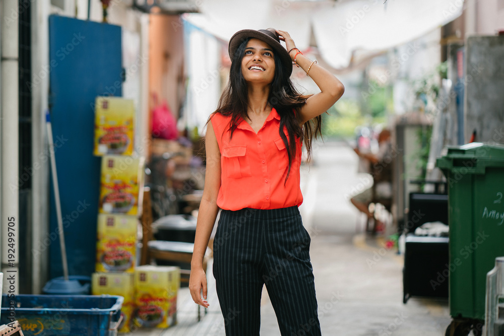 Young attractive professional Indian Asian lady standing in an alley while wearing a fedora hat during the day and enjoying the backstreets of Singapore.
