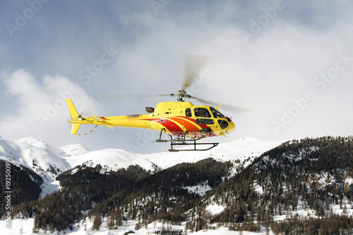 A yellow helicopter flying up in the air over the small town in Engadin St moritz Switzerland in the alps  for sightseeing in winter