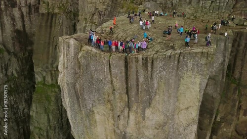 Aerial view from drone on breathtaking cliff called Preikestolen. Group of young people is standing on the edge of cliff and making the waves with hands. 4k footage, upper view. Norway.