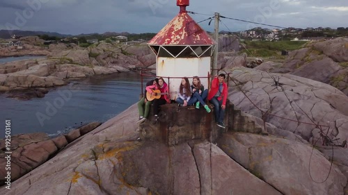 Aerial view from drone on beautiful lighthouse during sunset. Group of people enjoying evening on the rocks. 4k footage. Norway.