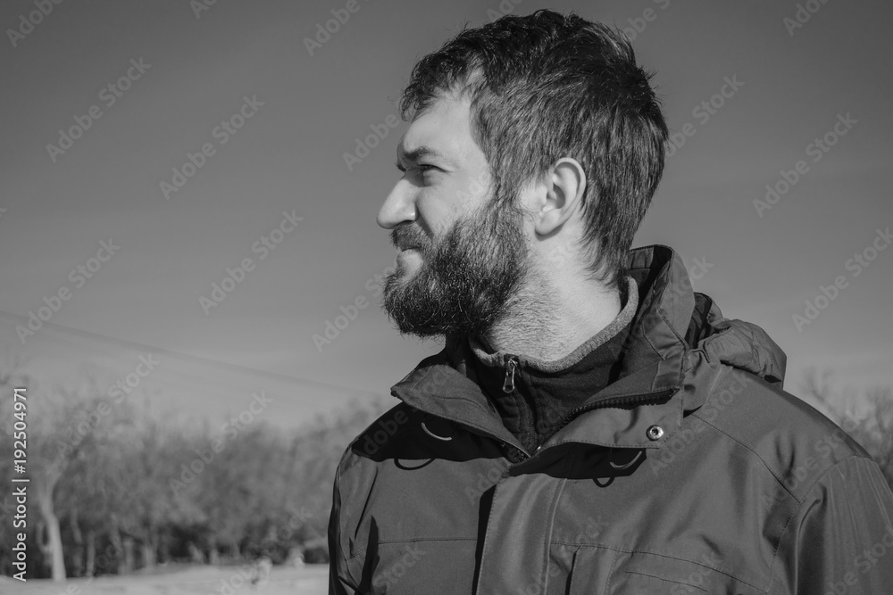 Obraz premium Portrait of a handsome pensive young man with a beard looks into the distance. dreaming guy on the background of blue sky and field. sunny day