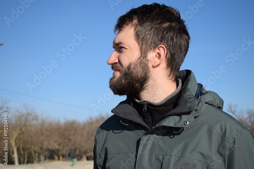 Portrait of a handsome pensive young man with a beard looks into the distance. dreaming guy on the background of blue sky and field. sunny day