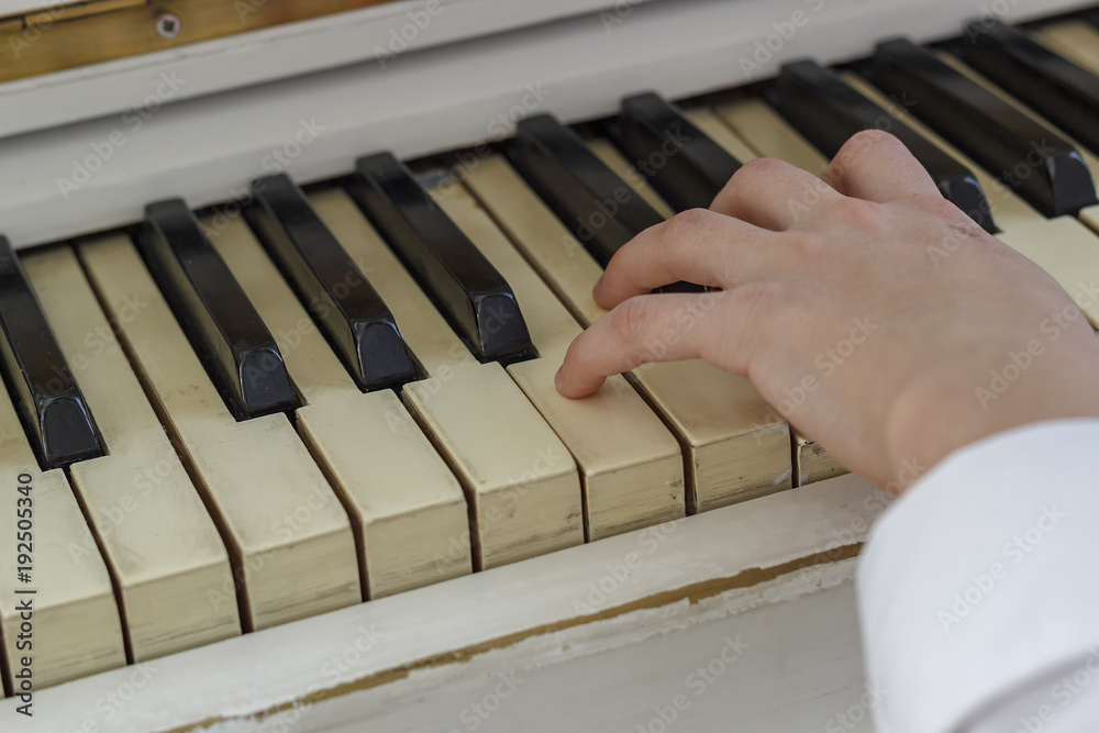 Fototapeta premium Hands of a young girl playing on a white piano, close-up.