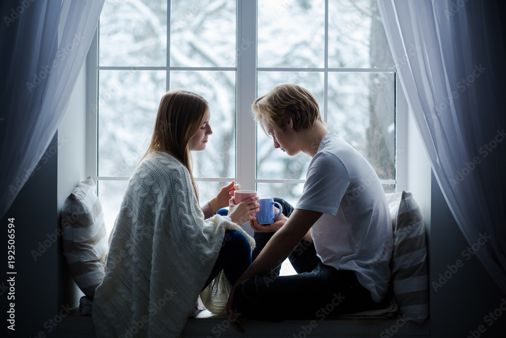 Obraz premium Young people sitting on a window-sill. They are giong to exchange their cups.