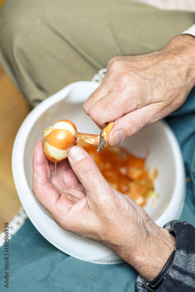 Senior elderly man peeling onion skin with a small sharp knife, preparing ingredients for lunch Senior elderly man peeling onion skin with a small sharp knife, preparing ingredients for lunch