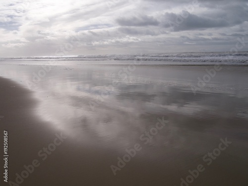 Stormy sky  at sunset  reflected on the surface of the water tide on a sandy Atlantic beach with the sun illuminating white waves  in winter in South West France  near Lacanau