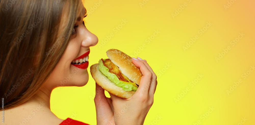 Woman with long hair holding burger standing back. Woman with long hair holding burger standing back.