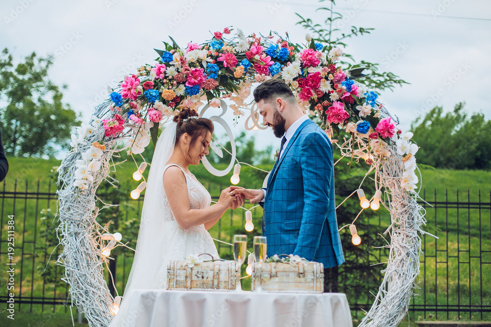 Two lovers hearts on the wedding ceremony. wonderful stylish rich happy bride and groom put ring at a weddings in green garden near white arch with flowers
