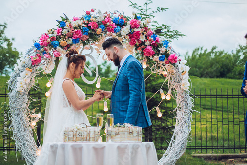 Two lovers hearts on the wedding ceremony. wonderful stylish rich happy bride and groom put ring at a weddings in green garden near white arch with flowers 
