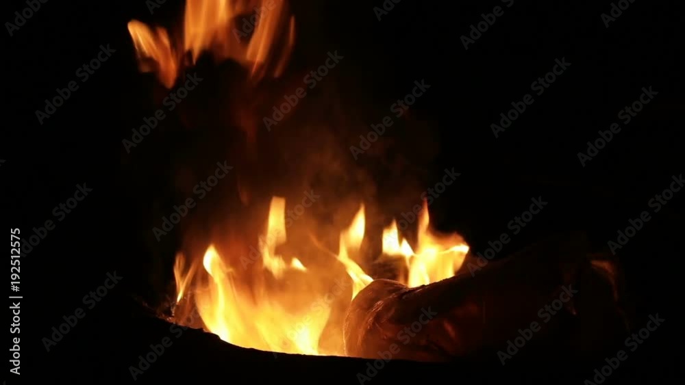 The carpet burns in a round garbage can at night. close-up.