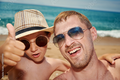Father and son are taking a selfie photo while having a rest on the beach.