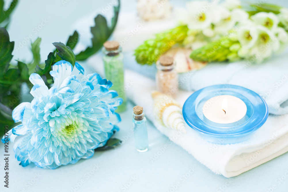 Aromatherapy spa concept with essential oil in blue glass bottle, sea salt, towel, candle, flowers and sea shells on blue background, instagram