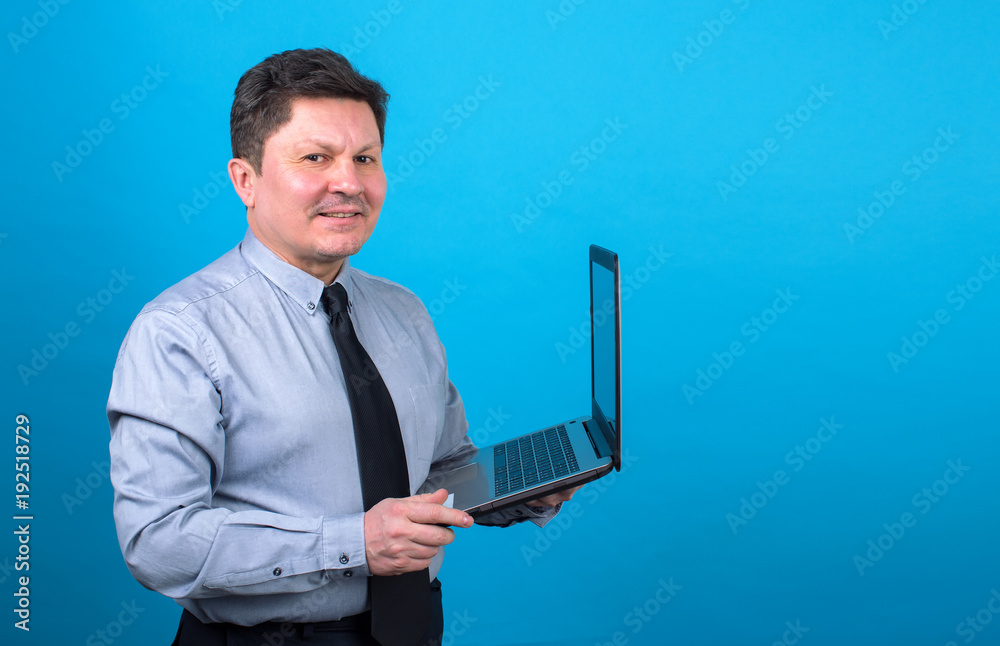 Middle aged business man with a laptop in hand on a blue background. Place for text. Middle aged business man with a laptop in hand on a blue background. Place for text.