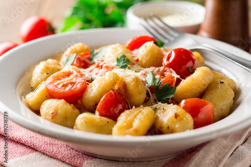 Homemade italian gnocchi with tomato, garlic, parsley and parmesan cheese on wooden table.