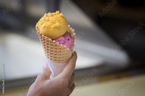 Waffle cone of two colored ice cream balls, pink and yellow colors, in woman's hand. Delicious cooling portion of sweet dessert on hot day and just for fun