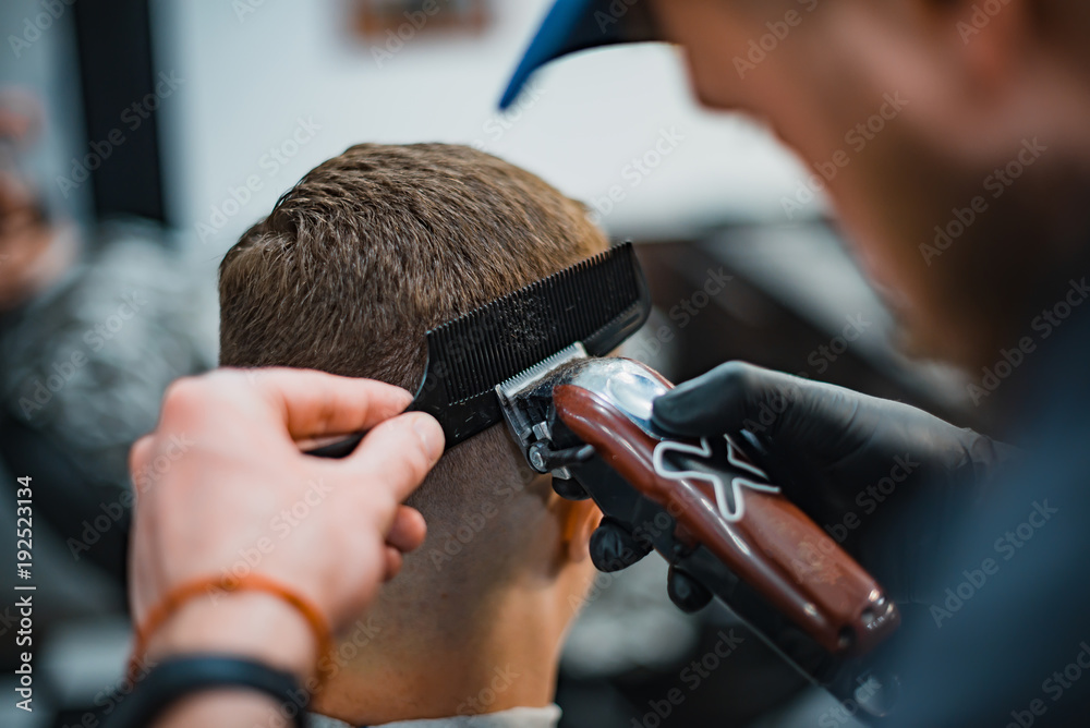 Man gets a cool haircut in barbershop. Barber makes the cut man electric razor. Men's care head. Soft focus. Man gets a cool haircut in barbershop. Barber makes the cut man electric razor. Men's care head. Soft focus.