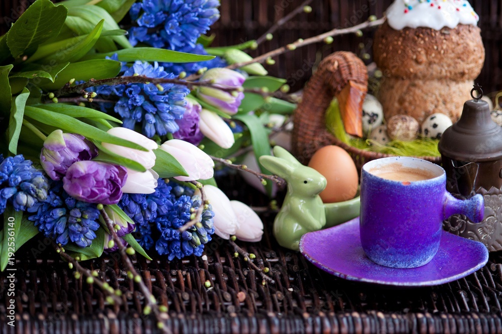 a bunch of spring flowers in lilac tones, and a cup of coffee with Easter bread and eggs, Easter
