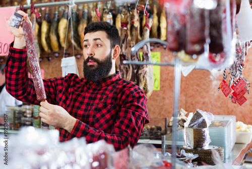 Young male customer examining sausages in butcher’s shop