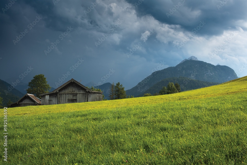 Grassy field with old wooden barn against mountain under thundercloud