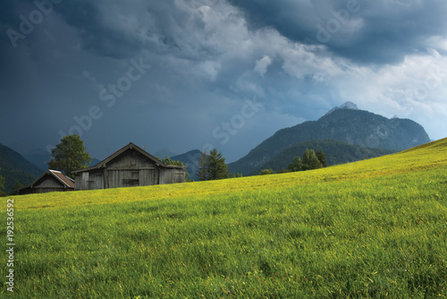 Grassy field with old wooden barn against mountain under thundercloud