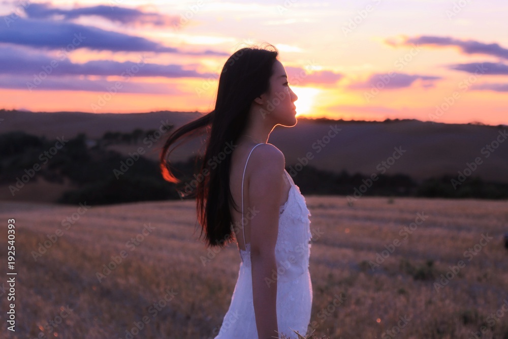 a silhouette of an Asian woman in white dress under sunset of Tuscany, Italy
