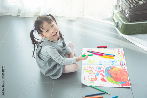 Little asian girl sitting on the floor and drawing picture by crayon and pencils
