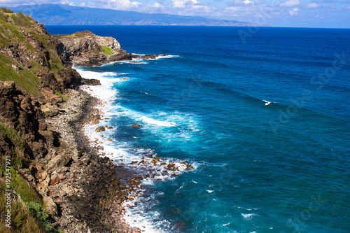 Volcanic rock, surf, and shades of the blue Pacific Ocean on the Maui coast, with the island of Molokai in the background