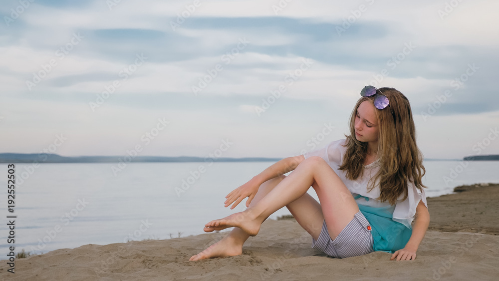 One beautiful teenage girl with brown hair outside on a beautiful summer day. A girl is doing herself a foot massage. Rubbing cream from sunburn. Sunburns are visible on the feet. One beautiful teenage girl with brown hair outside on a beautiful summer day. A girl is doing herself a foot massage. Rubbing cream from sunburn. Sunburns are visible on the feet.