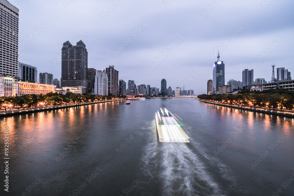Tour boat, captured with blurred motion, sails on the Pearl river that crosses the Guangzhou downtown district in Guangdong province in China at twilight