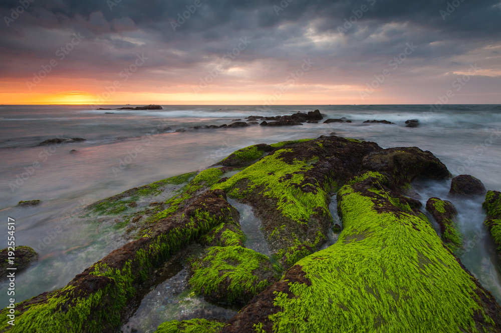 colorful sunset seascape with waves trails and green moss  at Kudat Sabah Malaysia. image contain soft focus due to long expose.