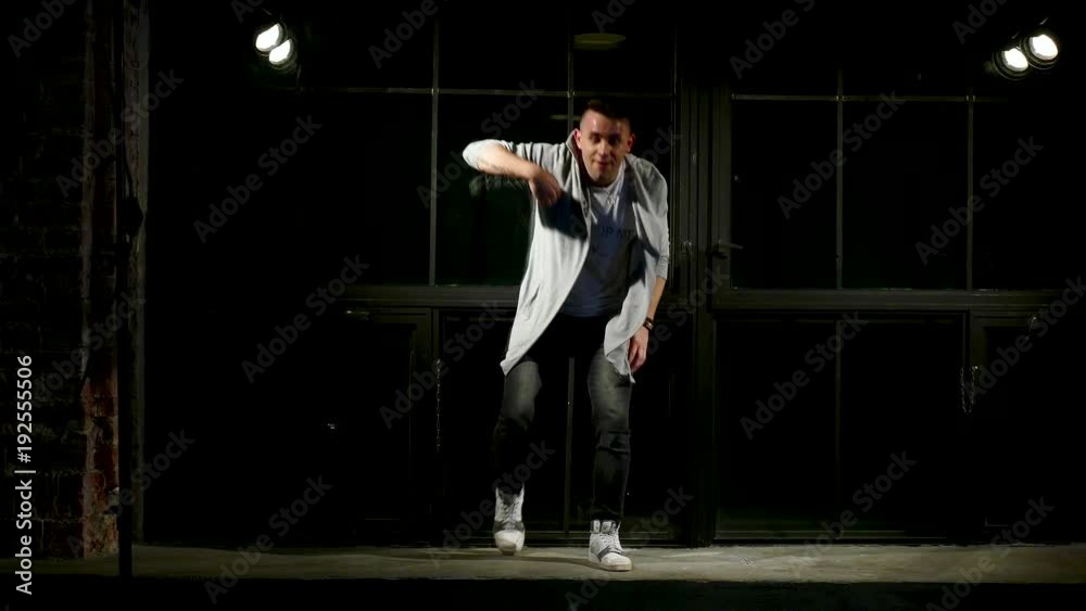 Man in black clothes dances in modern style on plinth near large window woth stage light Man in black clothes dances in modern style on plinth near large window woth stage light