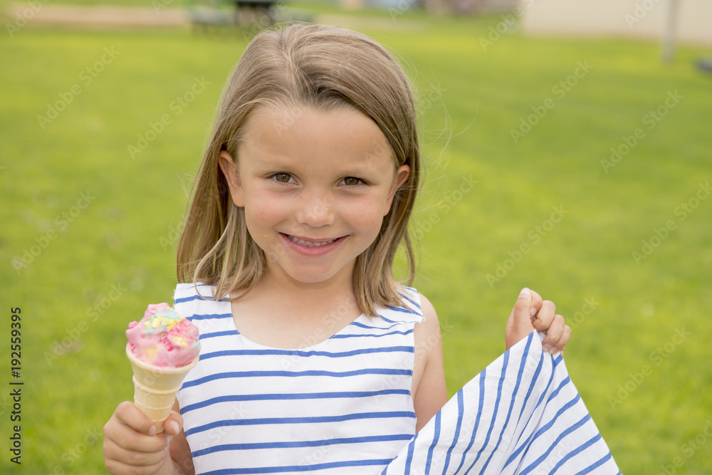 adorable and beautiful blond young girl 6 or 7 years old eating delicious ice cream smiling happy isolated on green grass field background adorable and beautiful blond young girl 6 or 7 years old eating delicious ice cream smiling happy isolated on green grass field background