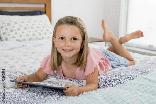 sweet and beautiful blond 6 or 7 years old young girl lying on bed smiling happy using the internet on digital tablet pad watching and having fun photo