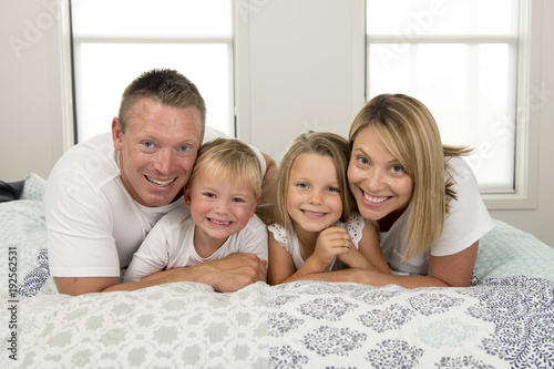 young beautiful and radiant couple 30 to 40 years old smiling happy posing sweet lying on bed with little son and beautiful daughter at home photo